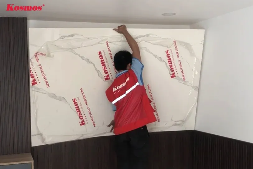 Áp sát tấm nhựa PVC vân đá đã bôi keo lên bề mặt tường phẳng, đảm bảo tấm được dán đều và chắc chắn.
