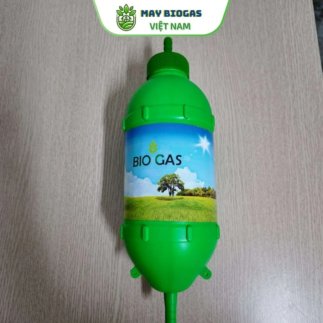 Bình lọc khí biogas dưới 20 khối màu xanh lá cây đặt trên nền cỏ, với các đầu nối ống và nhãn "BIO GAS"