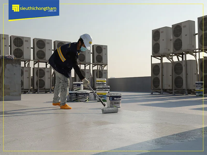 Thợ thi công quét lớp chống thấm chính trên bề mặt sàn mái đã chuẩn bị